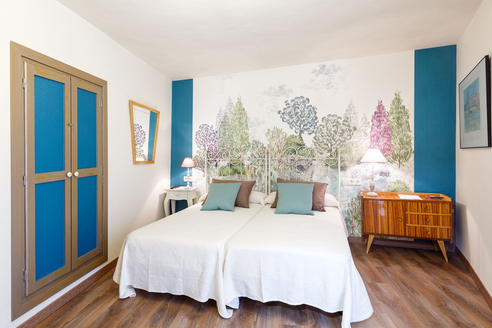Une chambre à coucher avec un lit double, une table de chevet, une commode et une grande fenêtre ornée d’une fresque murale.