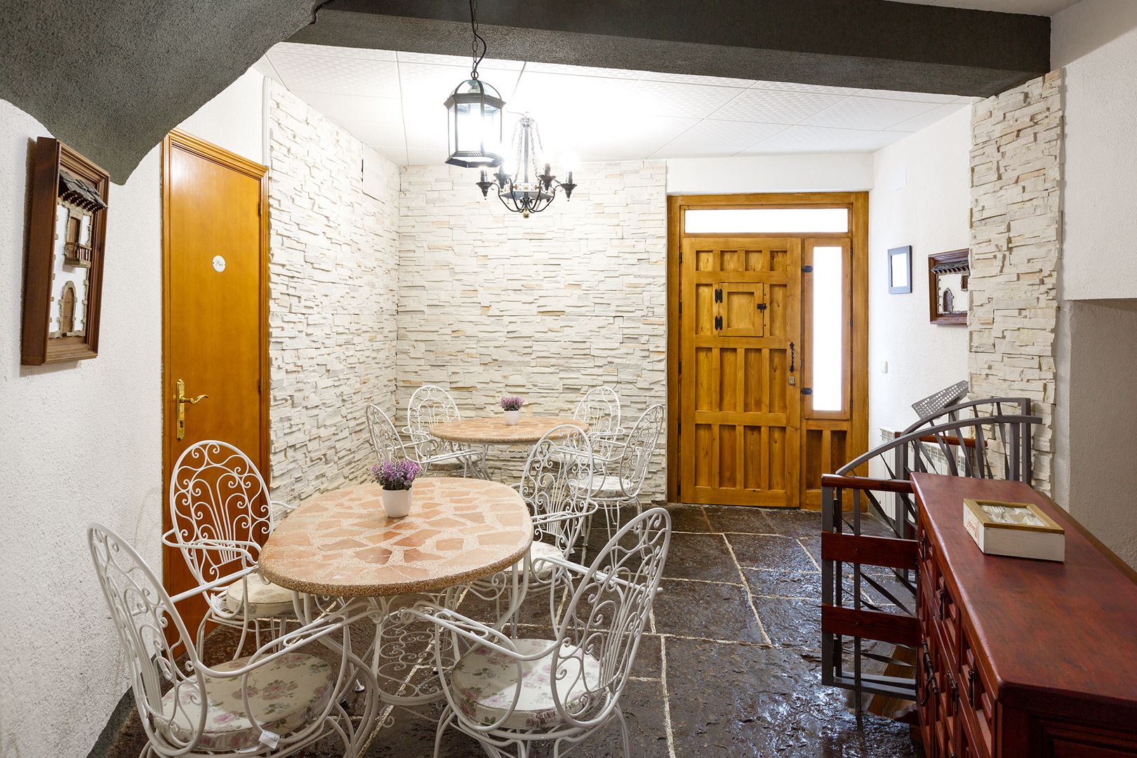 Un coin repas accueillant avec un mur en pierre, une porte en bois et des chaises en métal blanc disposées autour d’une table ronde.