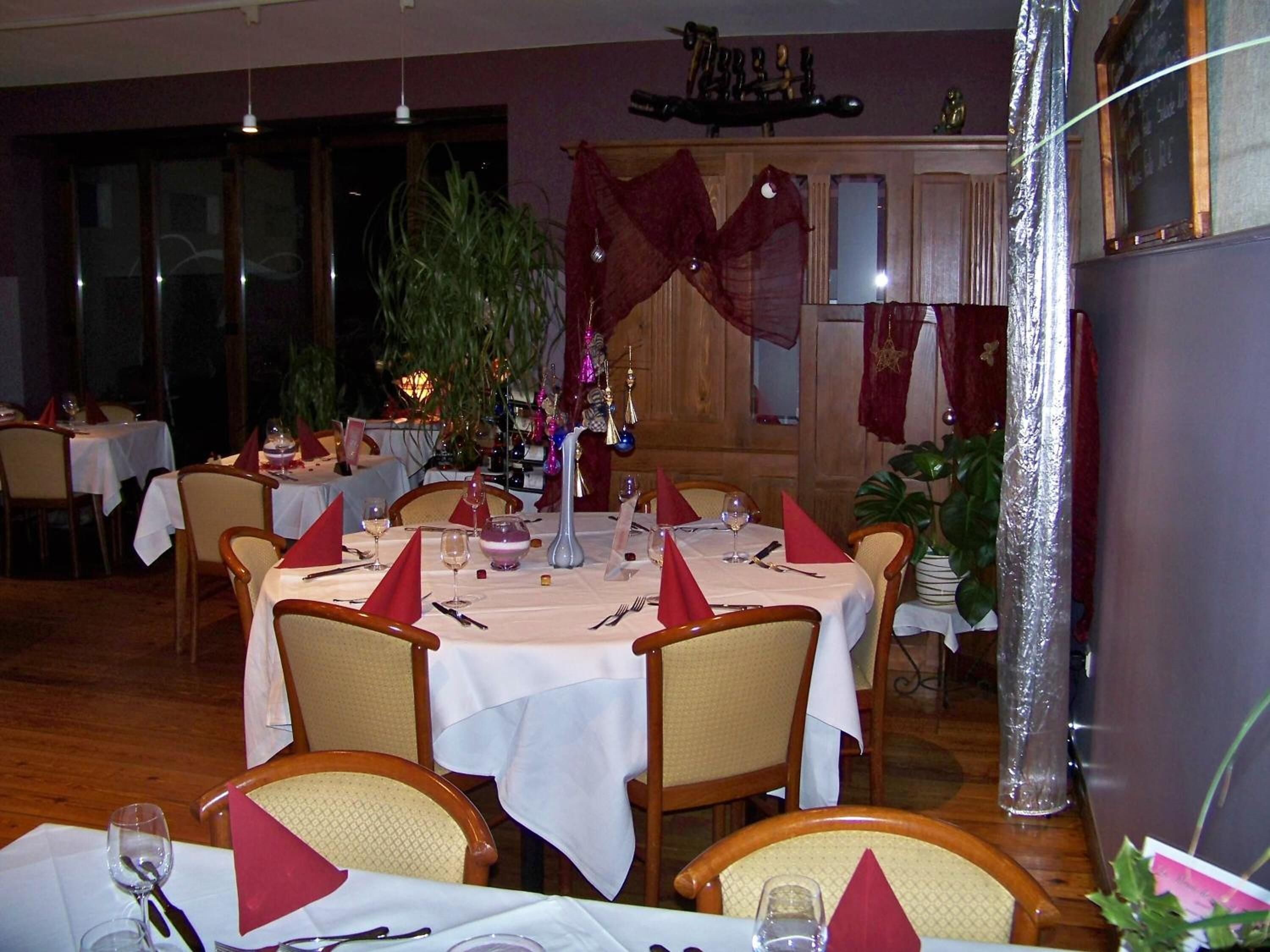Un restaurant avec des tables rondes dressées pour le repas, agrémentées de nappes blanches et de serviettes rouges.