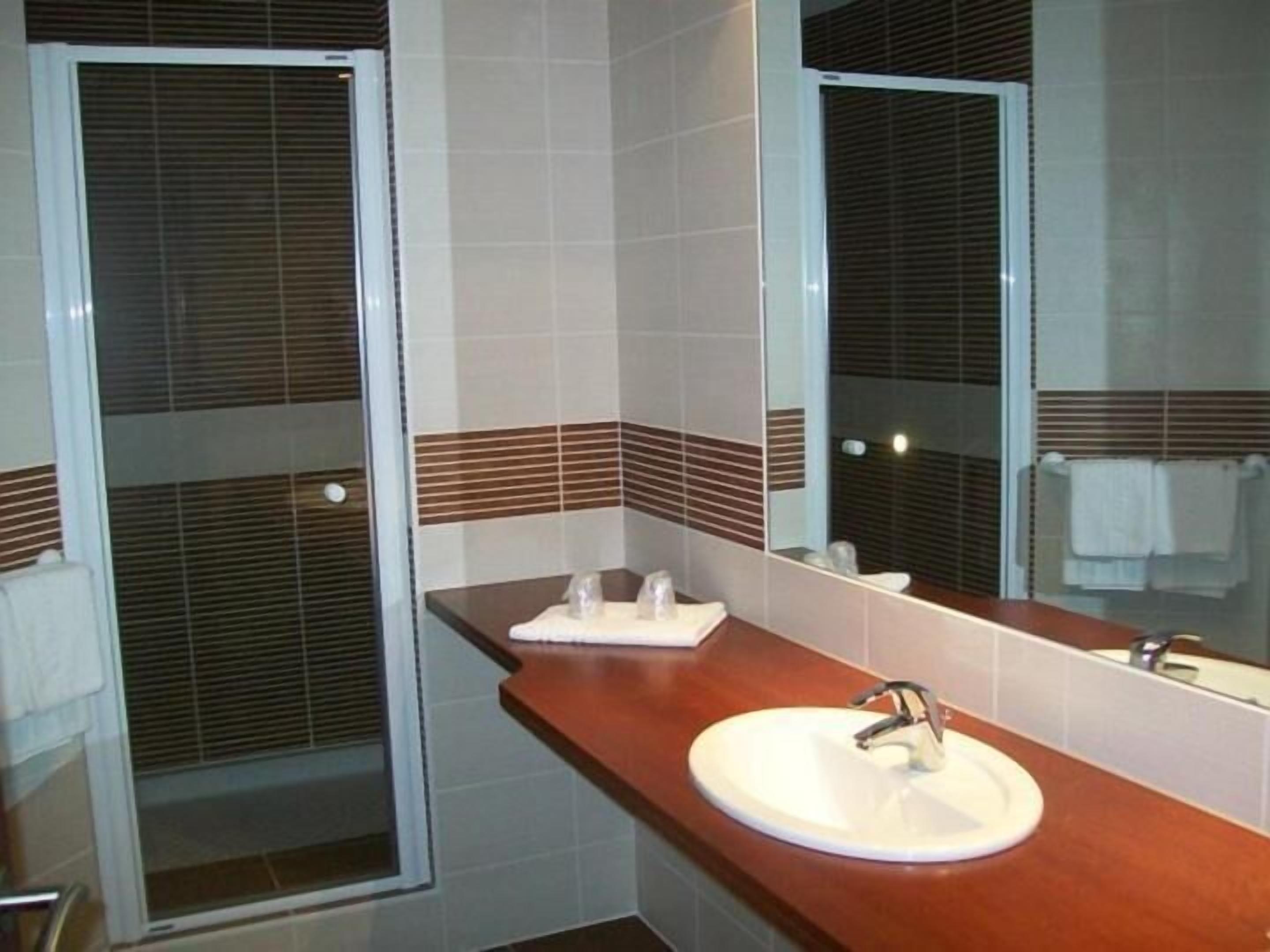 A bathroom with a white sink, a mirror, and a window with blinds.