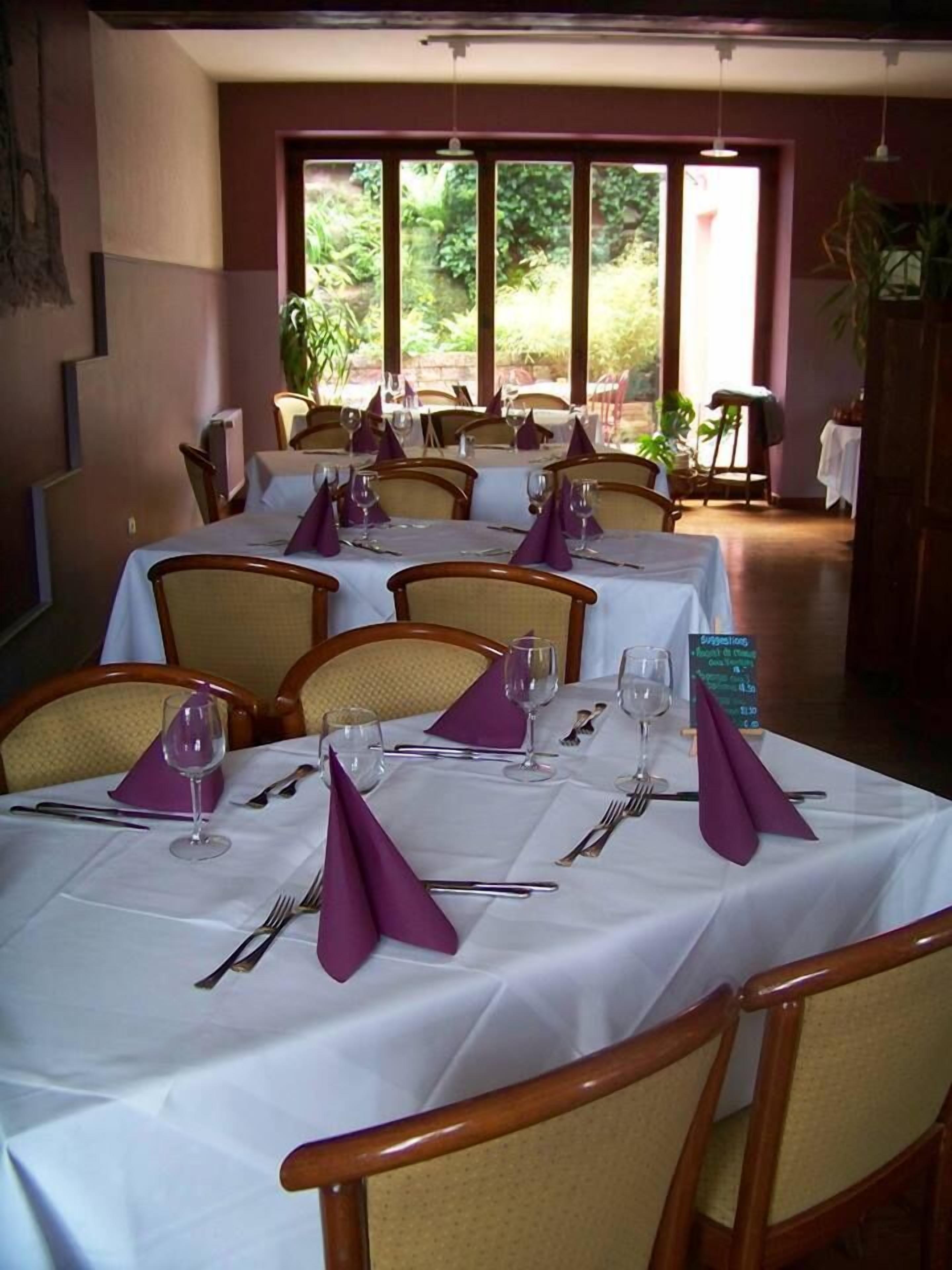 A dining area with tables set for four, each with white tablecloths, purple napkins, and silverware.