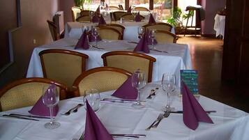 A dining area with tables set for four, each with white tablecloths, purple napkins, and silverware.