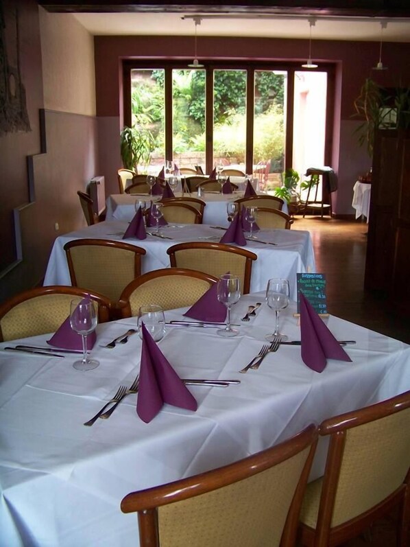 A dining area with tables set for four, each with white tablecloths, purple napkins, and silverware. - Hotel le Falken (Philippsbourg)