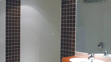 Ein Badezimmer mit Waschbecken in Weiß, dunklen Fliesenwänden und einem Holzbalken an der Decke.