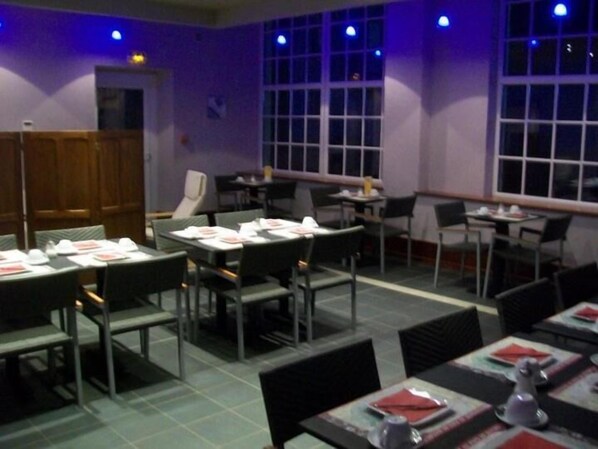 A restaurant with tables set for dining, chairs, and a window with blinds. - Hotel le Falken (Philippsbourg)