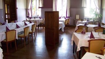A dining area with multiple tables set for service, wooden chairs, and a large wooden cabinet.