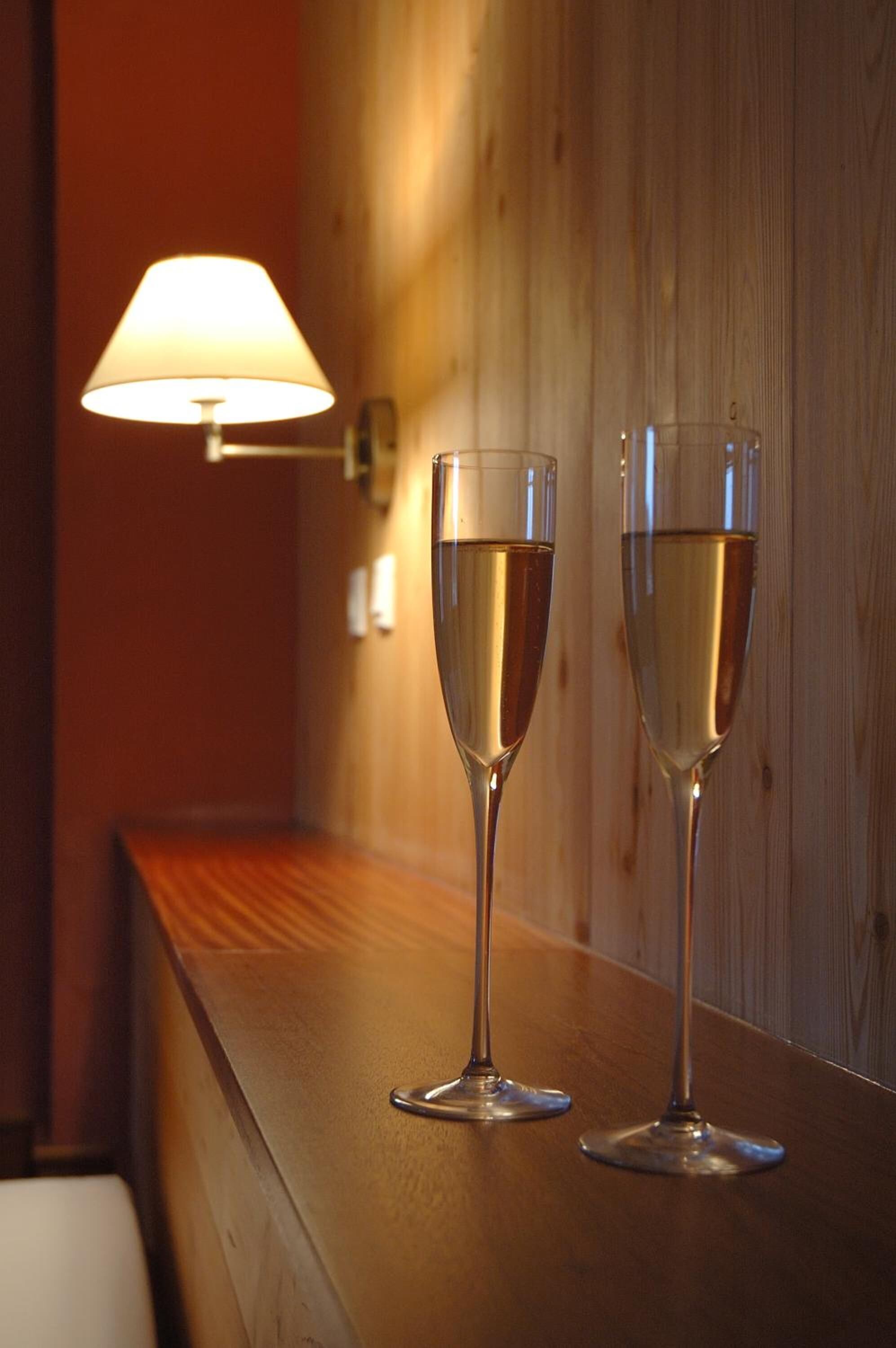 Two glasses of champagne on a wooden bar counter with a wall-mounted lamp in the background.