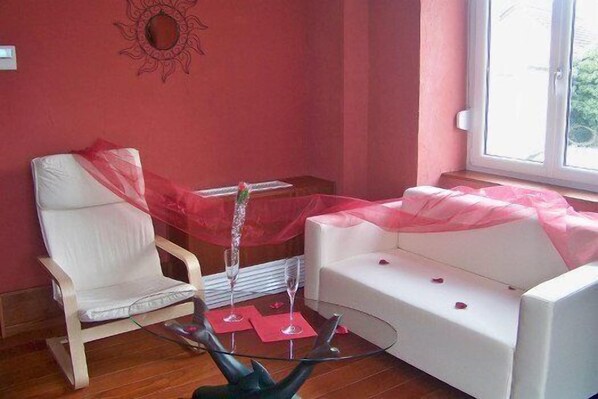 A room with a white chair, a white sofa, a glass coffee table, and a window with a view. - Hotel le Falken (Philippsbourg)