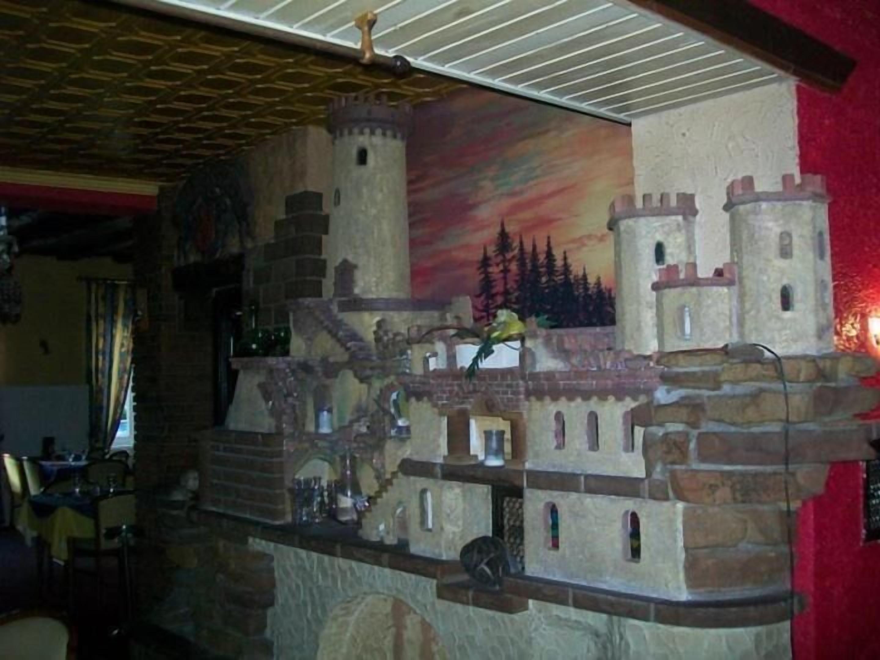 Une pièce dont un mur est décoré d’une fresque en pierre représentant un château, avec un plafond en bois et un mur rouge.