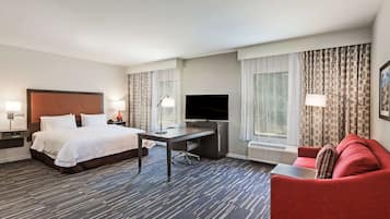 Ein Hotelzimmer mit Bett, Schreibtisch, Fernseher, einem roten Sofa und Vorhängen.
