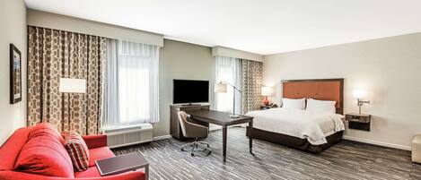 A hotel room with a bed, a desk, a chair, a TV, and a red sofa.