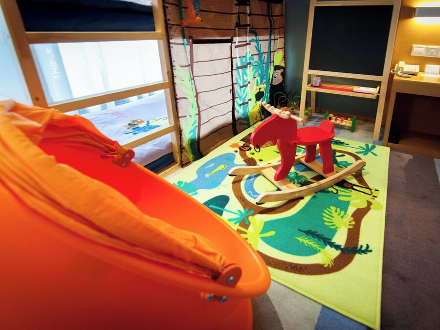 Zona de juegos para niños con un tapete de colores, un caballo de juguete y una cama con vistas al exterior.
