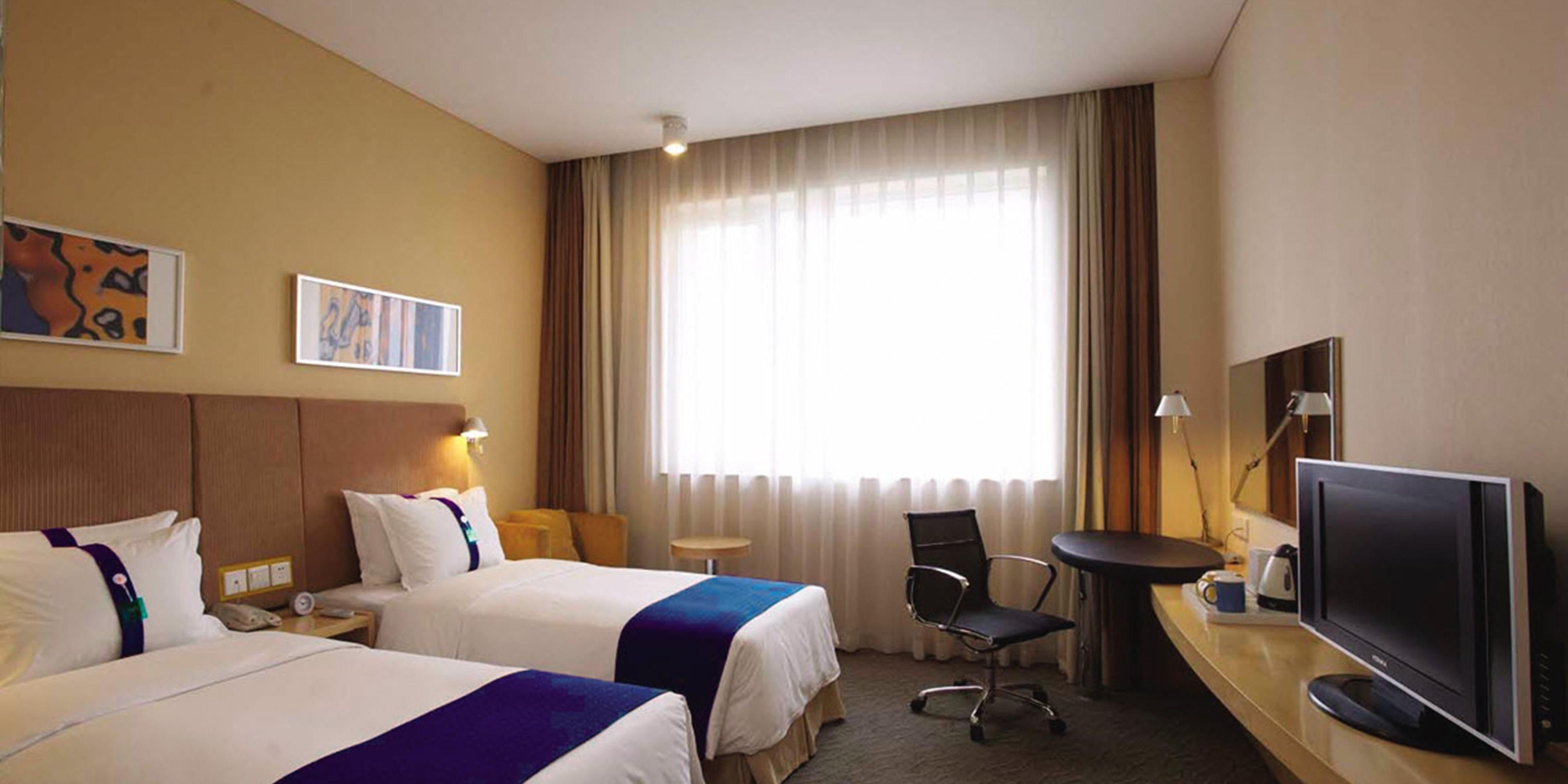 A hotel room with two beds, a desk with a computer, a chair, and a television.