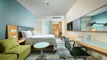 Une chambre d’hôtel moderne avec un lit, un canapé vert, un bureau avec une chaise et un grand miroir.