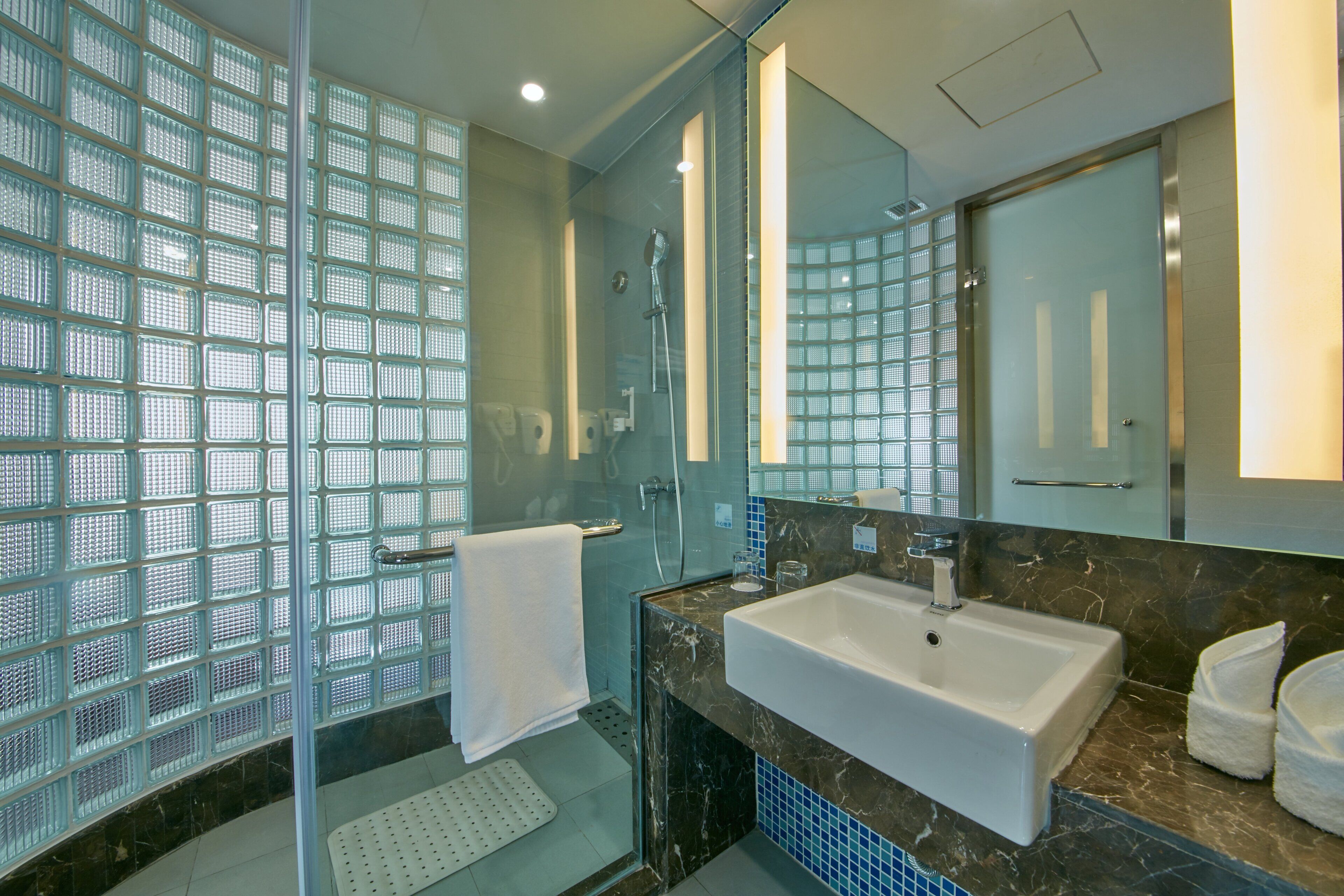 Un baño moderno con cabina de ducha de vidrio, un lavabo blanco y un espejo grande.