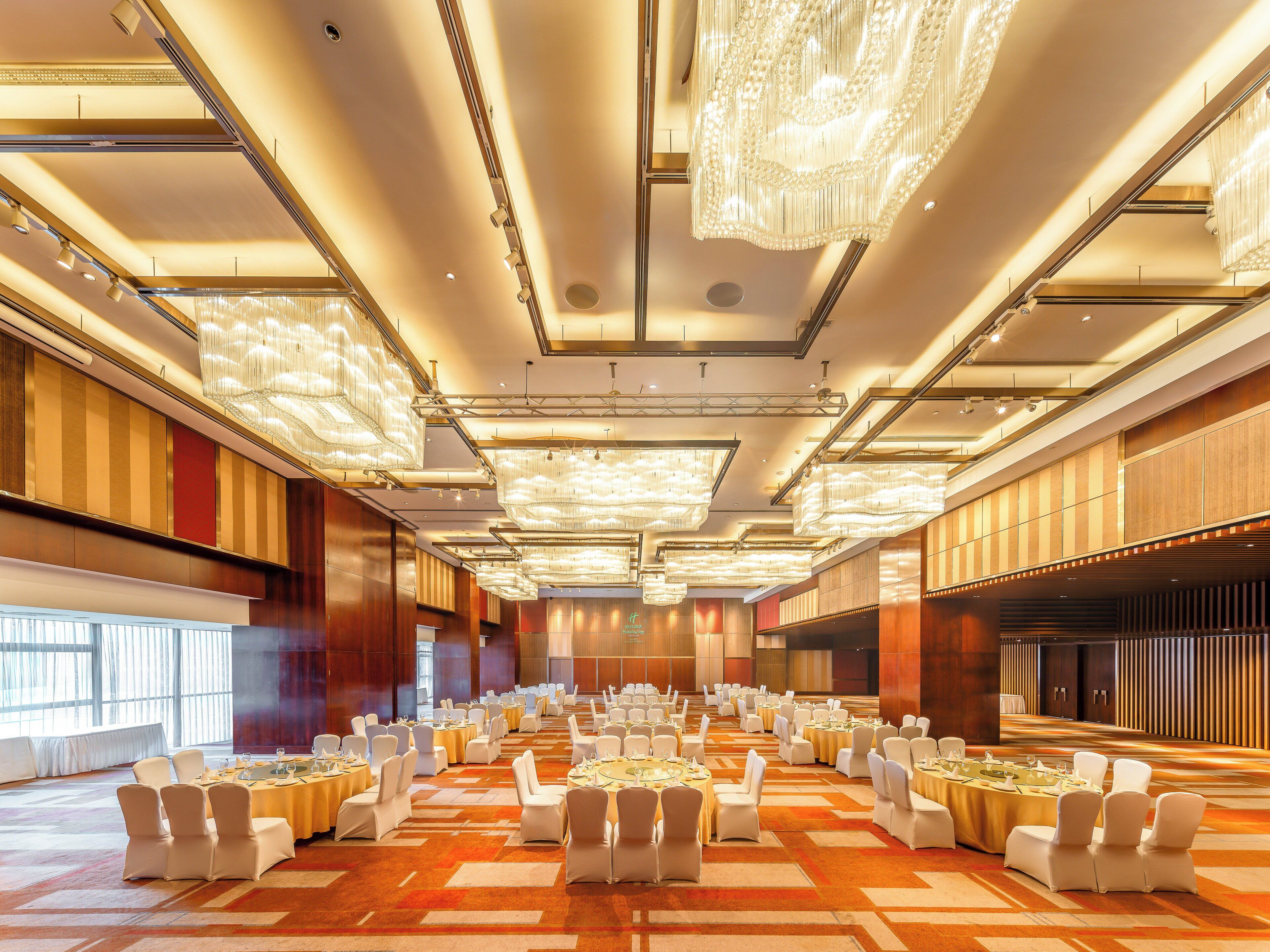 Un amplio salón de banquetes con varias mesas redondas, sillas blancas y candelabros.