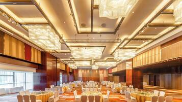 Un amplio salón de banquetes con varias mesas redondas, sillas blancas y candelabros.