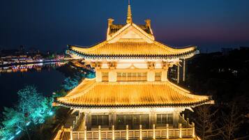 Un edificio japonés tradicional con un techo simétrico y varias ventanas, rodeado por una masa de agua y un paisaje urbano al fondo.