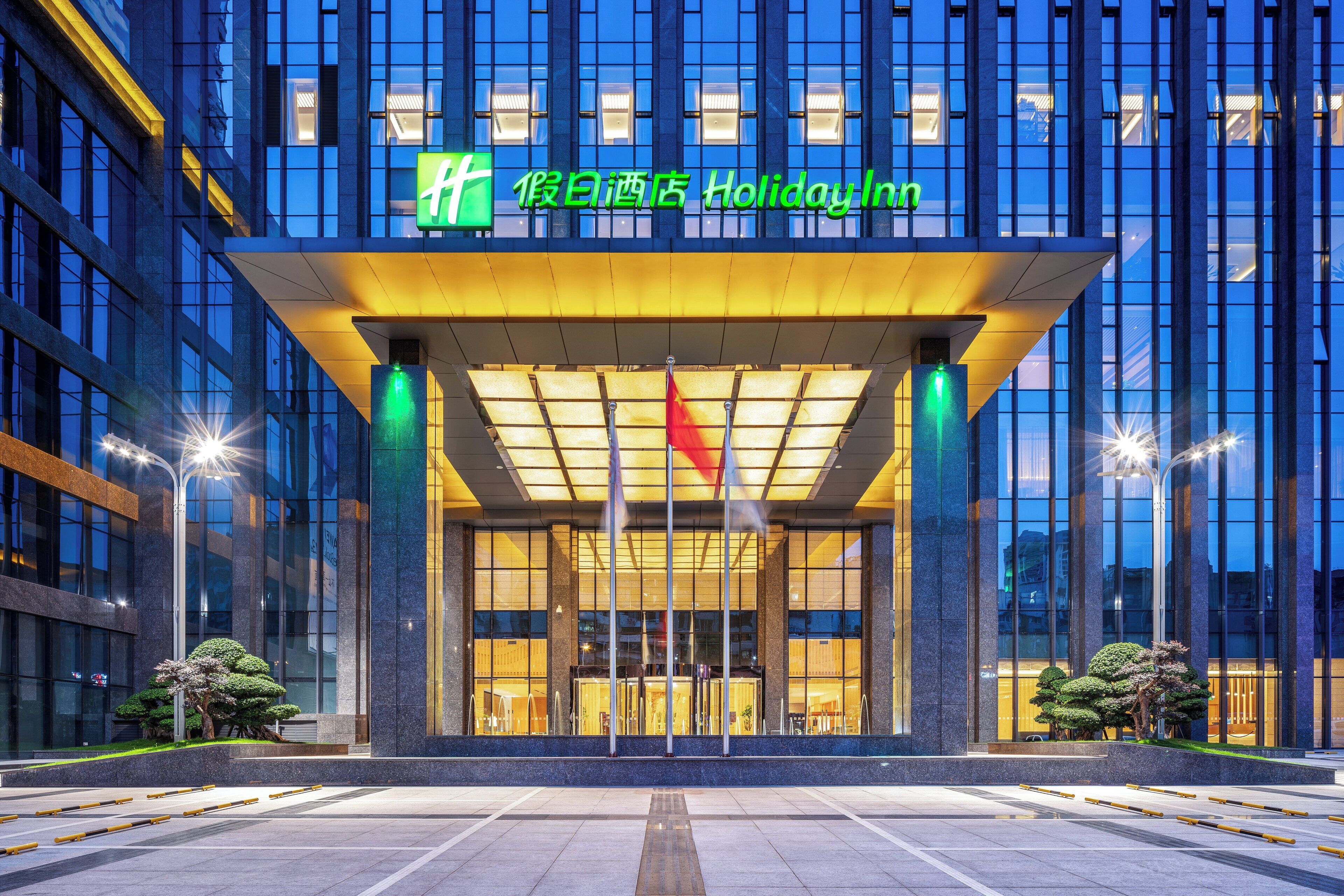 A modern hotel entrance with a glass facade and a prominent green sign.