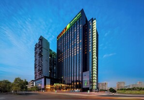 A modern hotel with a prominent 'Holiday Inn' sign, featuring a glass facade and a well-lit entrance.