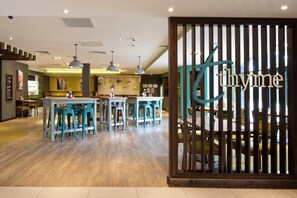 Ein Restaurantinneres mit Holzboden, blauen Barhocker, Pendelleuchten und einer Holzwand mit dem Wort 'thyme'.