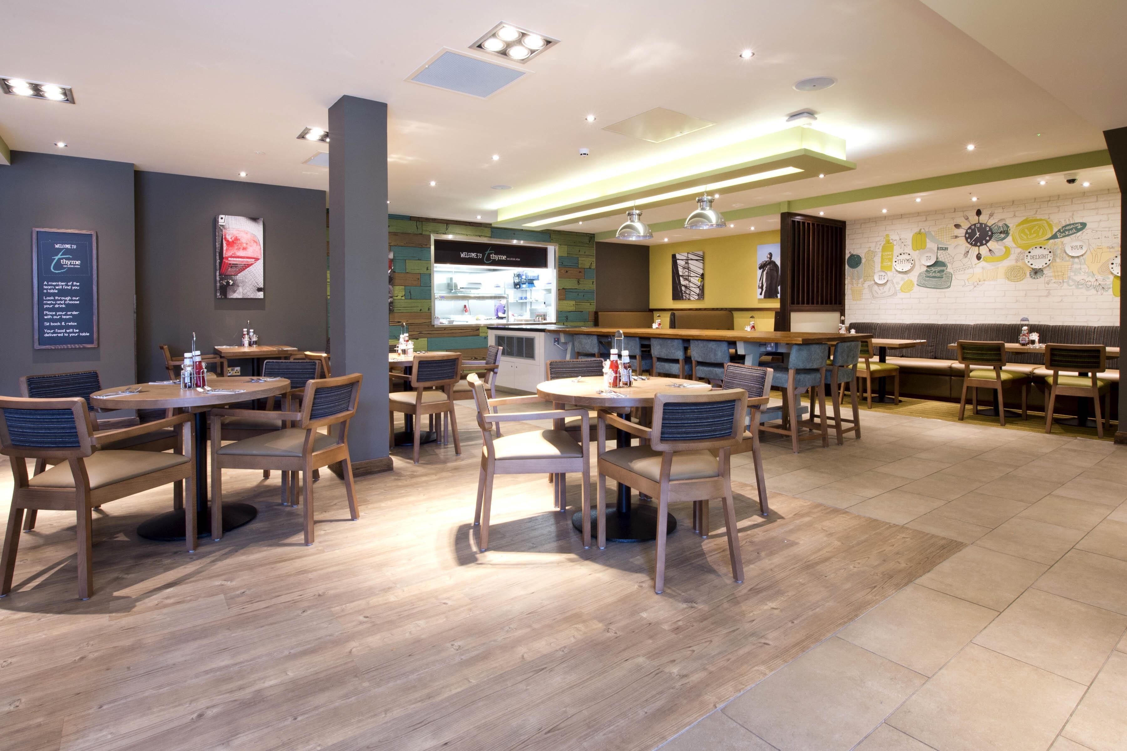 A restaurant with multiple seating areas, including round tables and booths, with a menu display and a wall with a clock and abstract art.