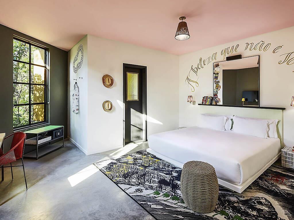 Un dormitorio con cama, escritorio, silla, ventana grande y pared decorada.
