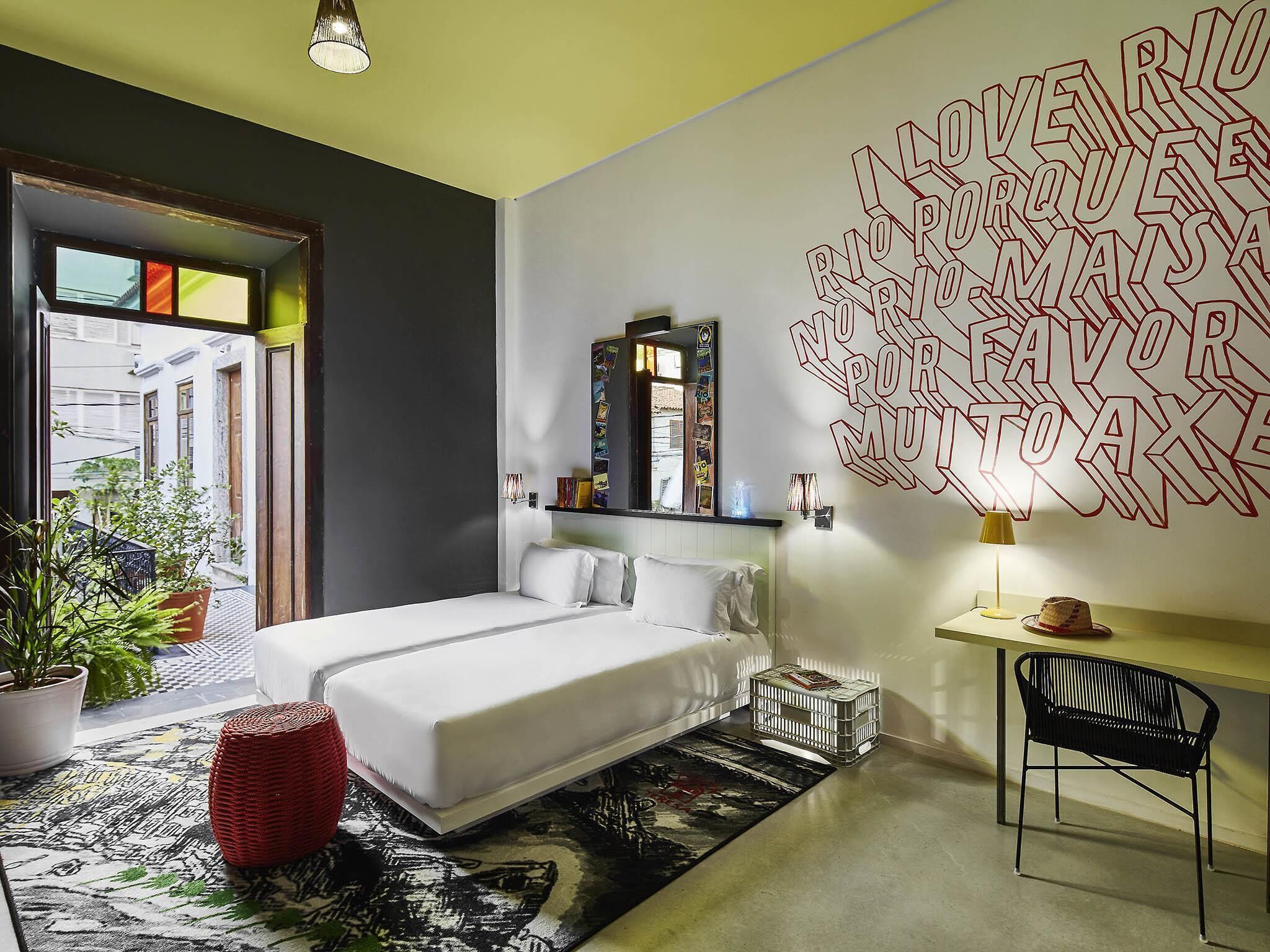 Un dormitorio moderno con cama, espejo, una obra de arte en la pared, escritorio y silla.