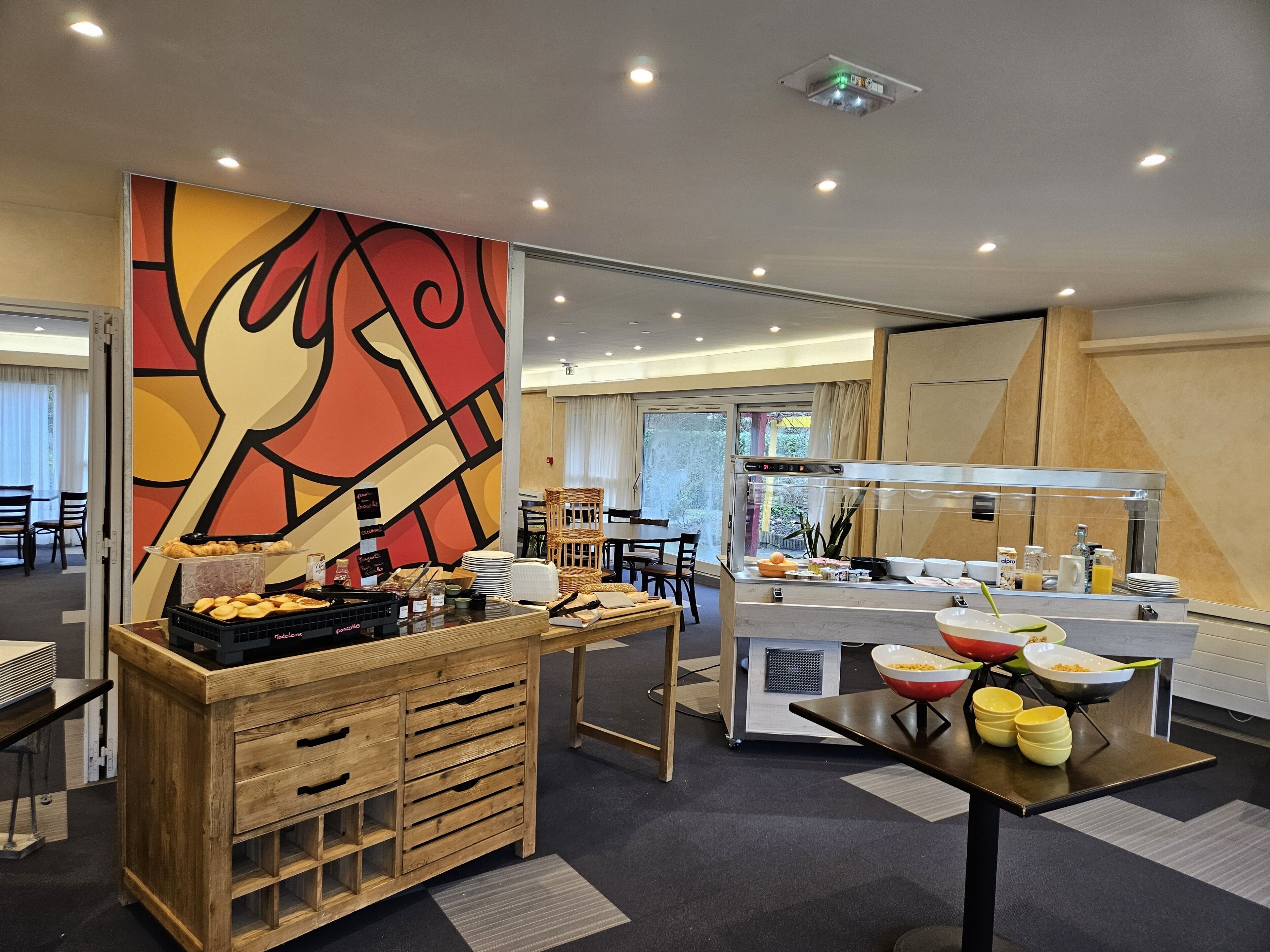 A buffet area with a variety of food items, a wooden counter with drawers, and a seating area with chairs and tables.