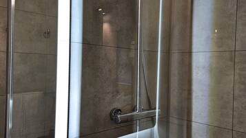 Un baño moderno con cabina de ducha de vidrio, espejo empotrado y lavamanos con dispensador de jabón.