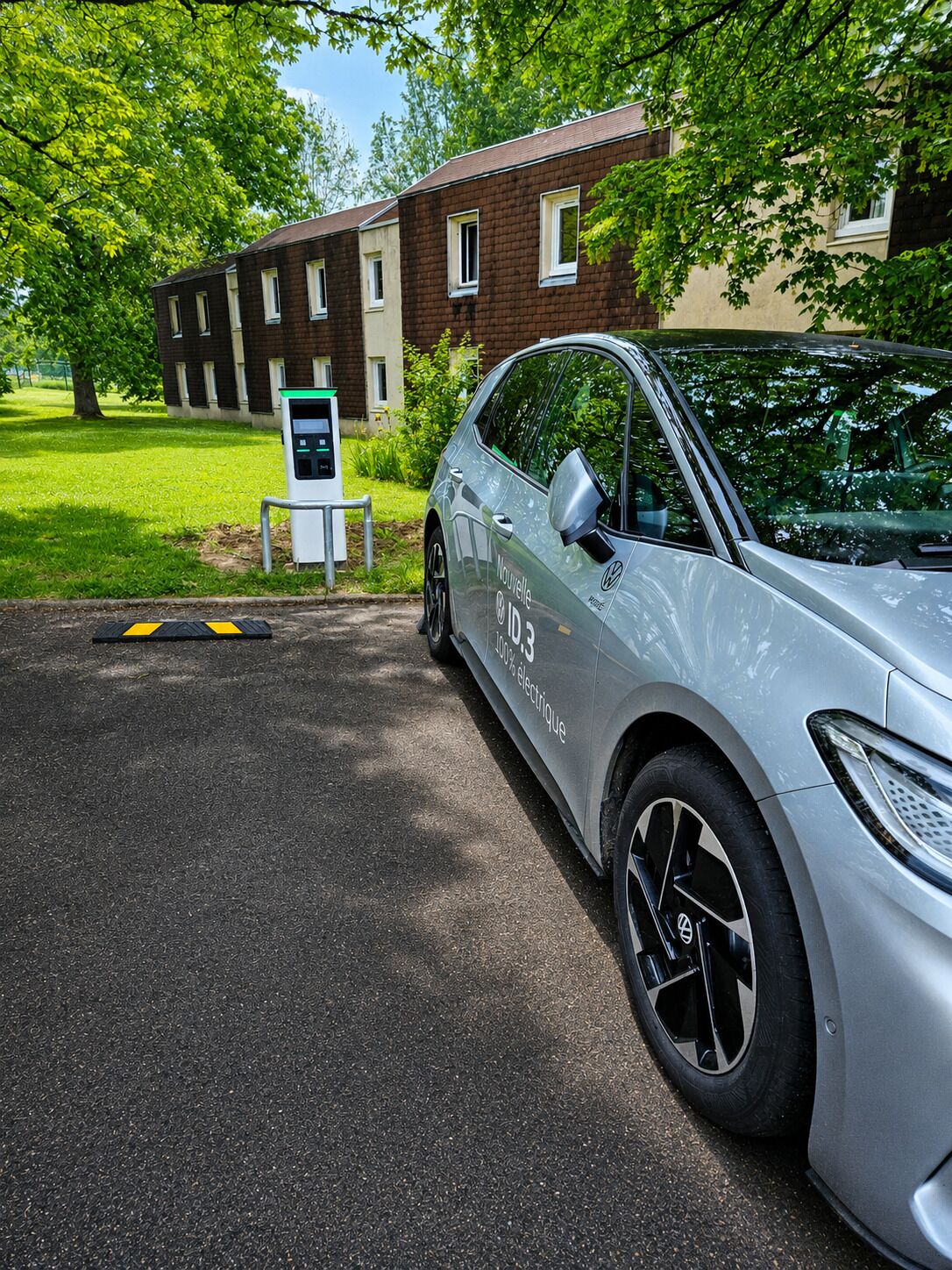 Un auto eléctrico plateado estacionado frente a un edificio con una estación de carga.