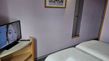 A hotel room with a bed, a desk with a computer, a framed picture on the wall, and a door.