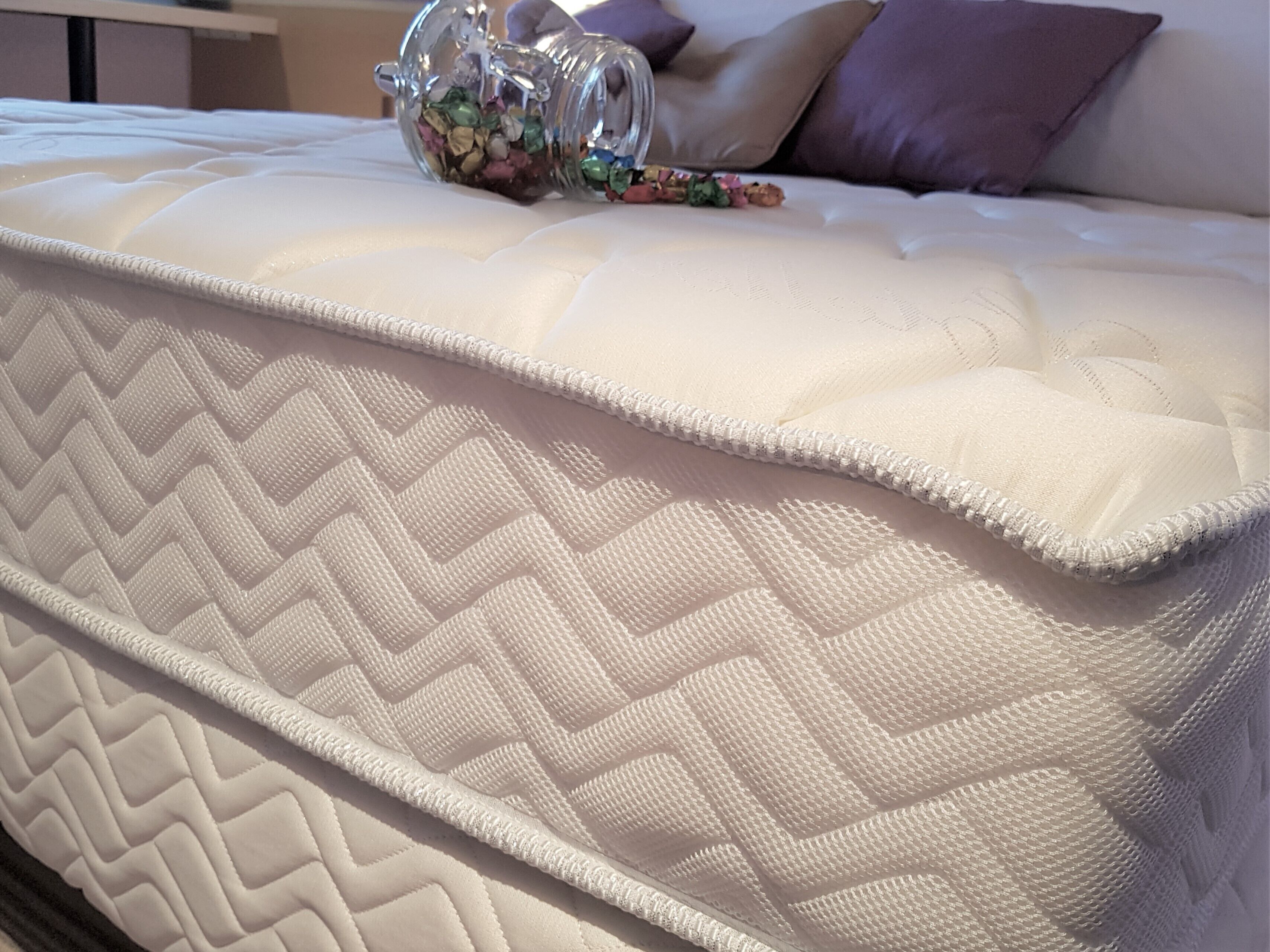 Una cama con un colchón acolchado y un tarro de vidrio decorativo encima.
