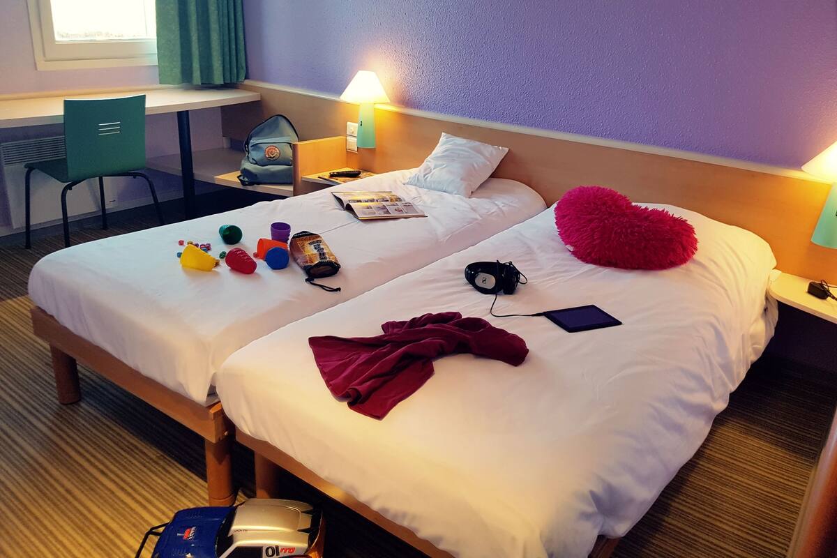 A hotel room with two beds, a desk, a chair, and a window with curtains.