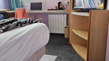 Quarto de hotel com cama, secretária com laptop, televisão e radiador.