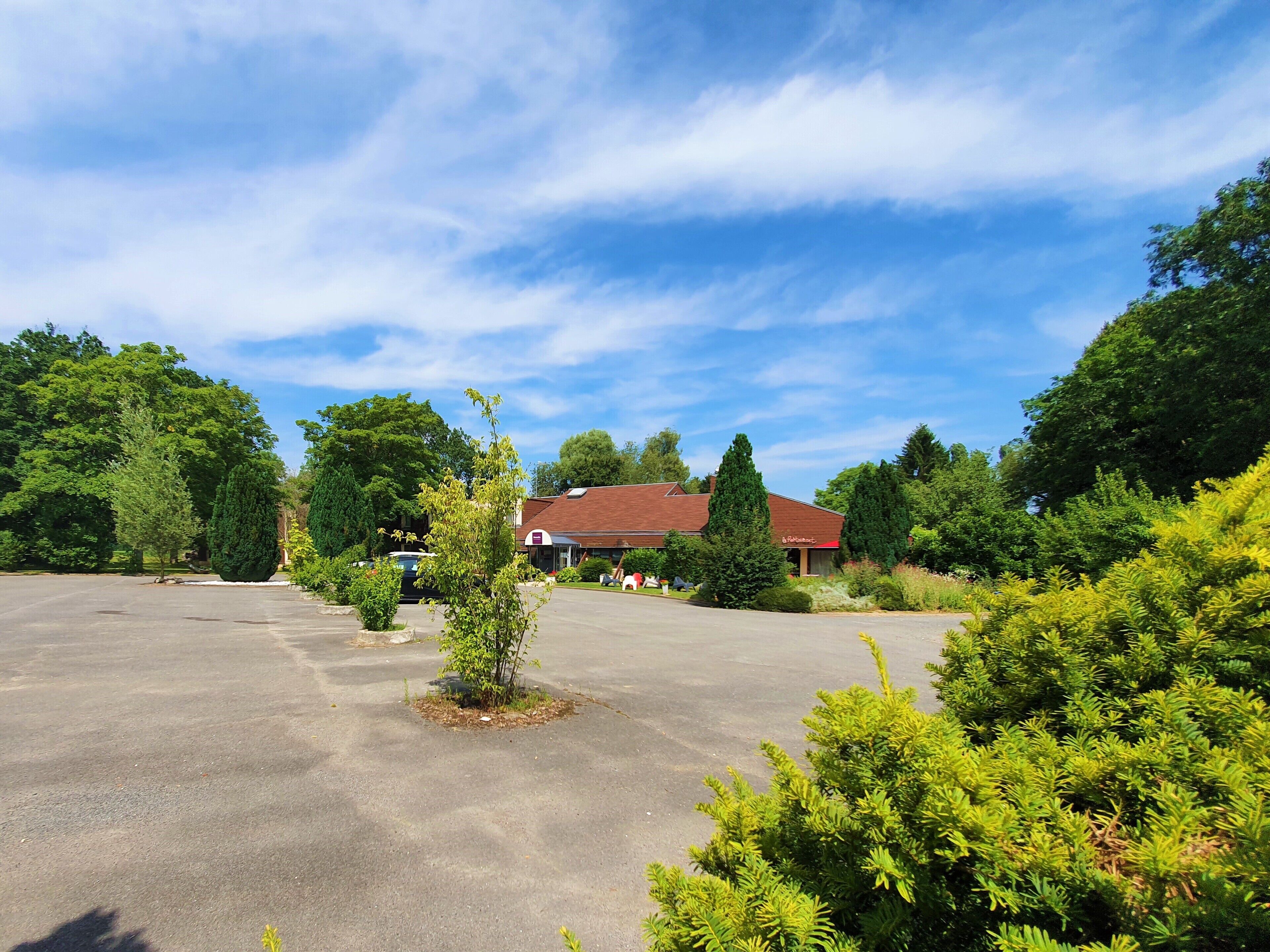 A large parking lot with a building in the background, surrounded by trees and greenery.