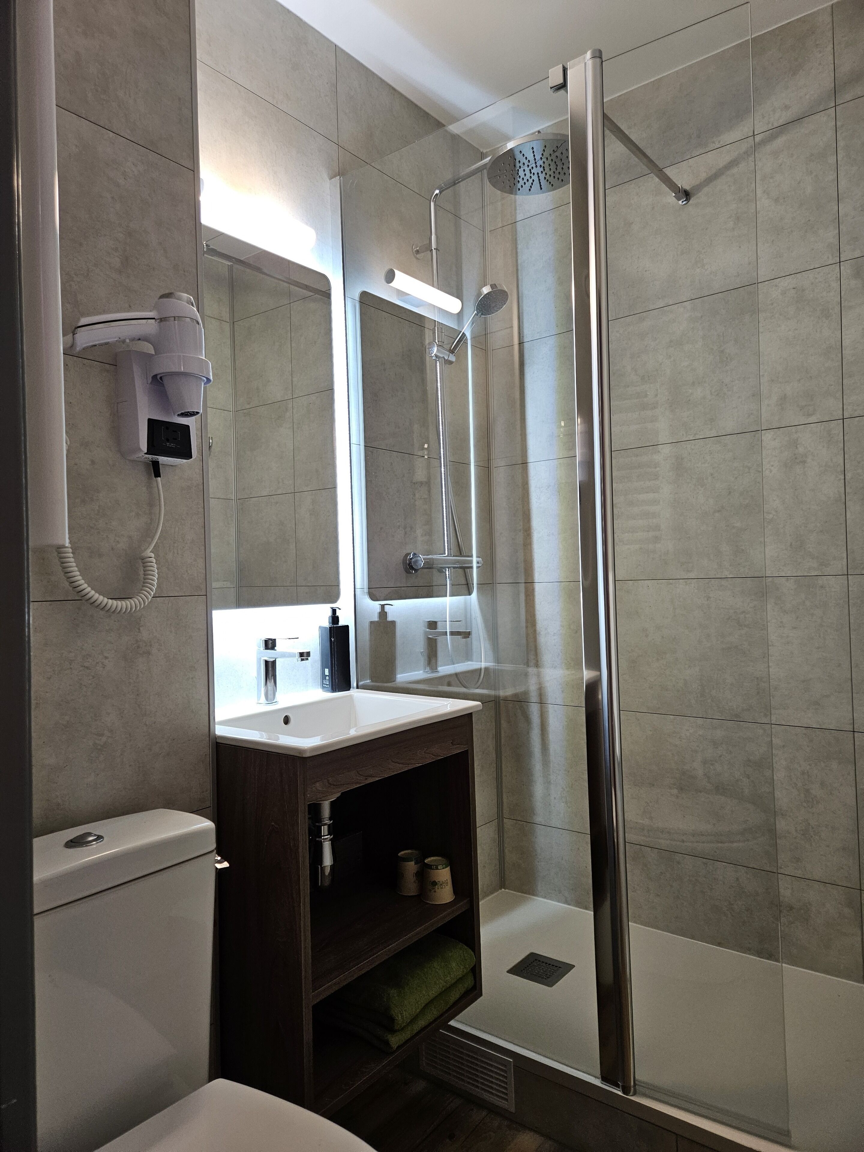 A modern bathroom with a glass-enclosed shower, a vanity with a mirror, and a hairdryer mounted on the wall.
