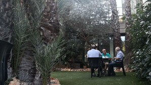 A group of people seated at a table in an outdoor garden area with lush greenery and a stone wall in the background. - Hotel 90 (Capurso)