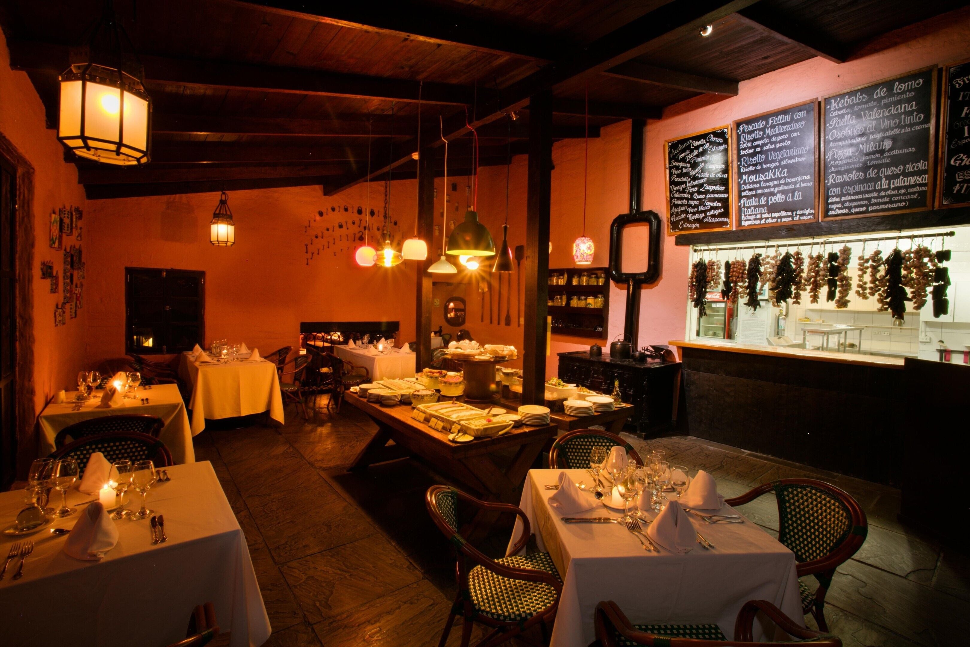 A restaurant interior with multiple tables set for dining, hanging pendant lights, and a menu board displaying food options.