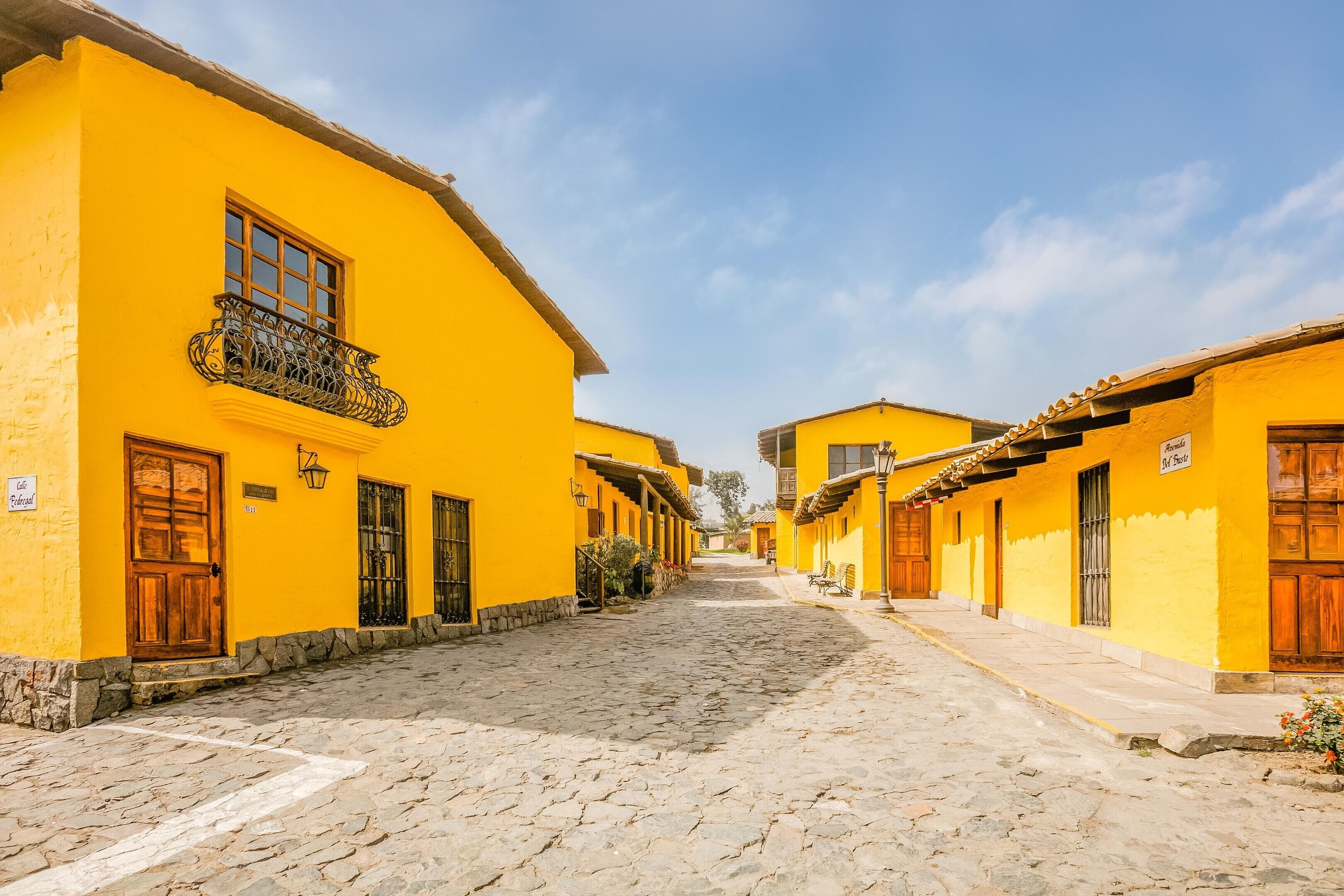 A cobblestone street lined with yellow buildings, each with a wooden door and window.