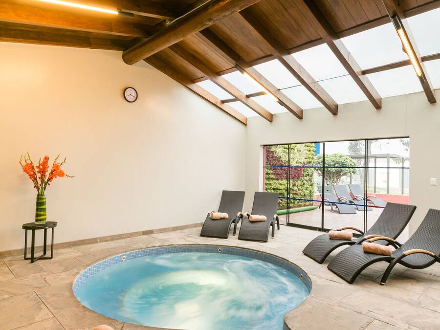 An indoor swimming pool with lounge chairs, a clock on the wall, and a vase with flowers.