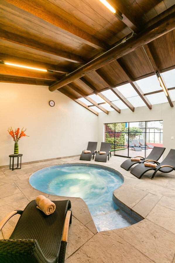 An indoor swimming pool with lounge chairs, a clock on the wall, and a vase with flowers. - Decameron El Pueblo - All Inclusive (Lima)