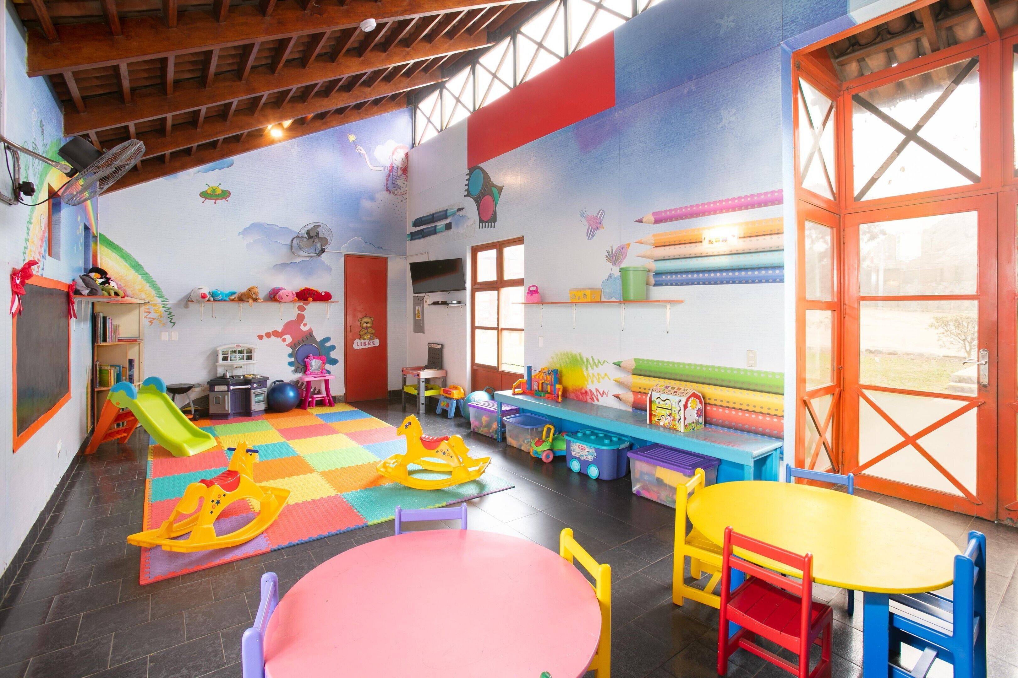 A children's playroom with a colorful floor, play mats, and various toys.