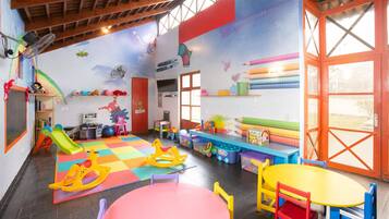 A children's playroom with a colorful floor, play mats, and various toys.