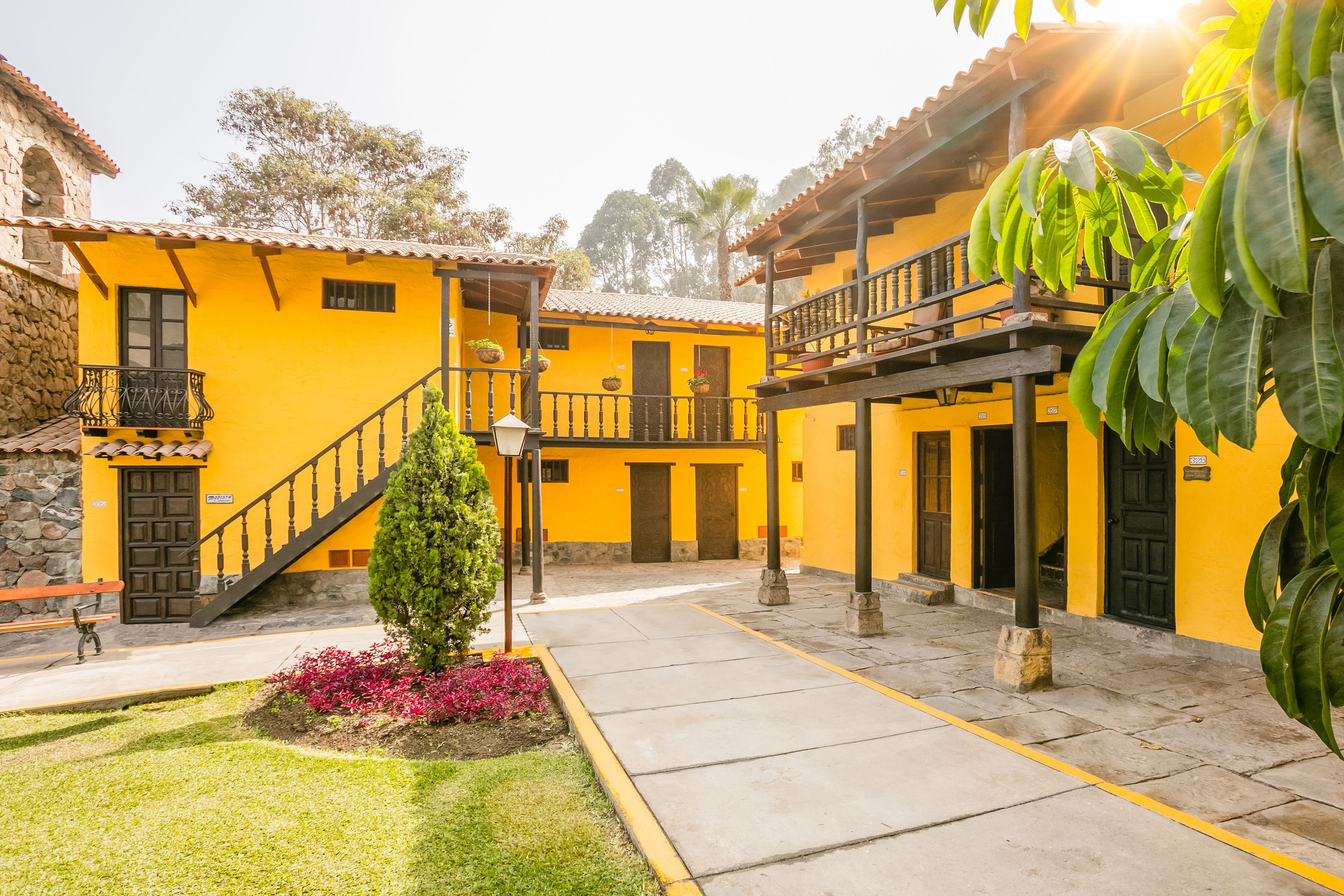 Un patio con edificios amarillos, una escalera y un pequeño árbol.