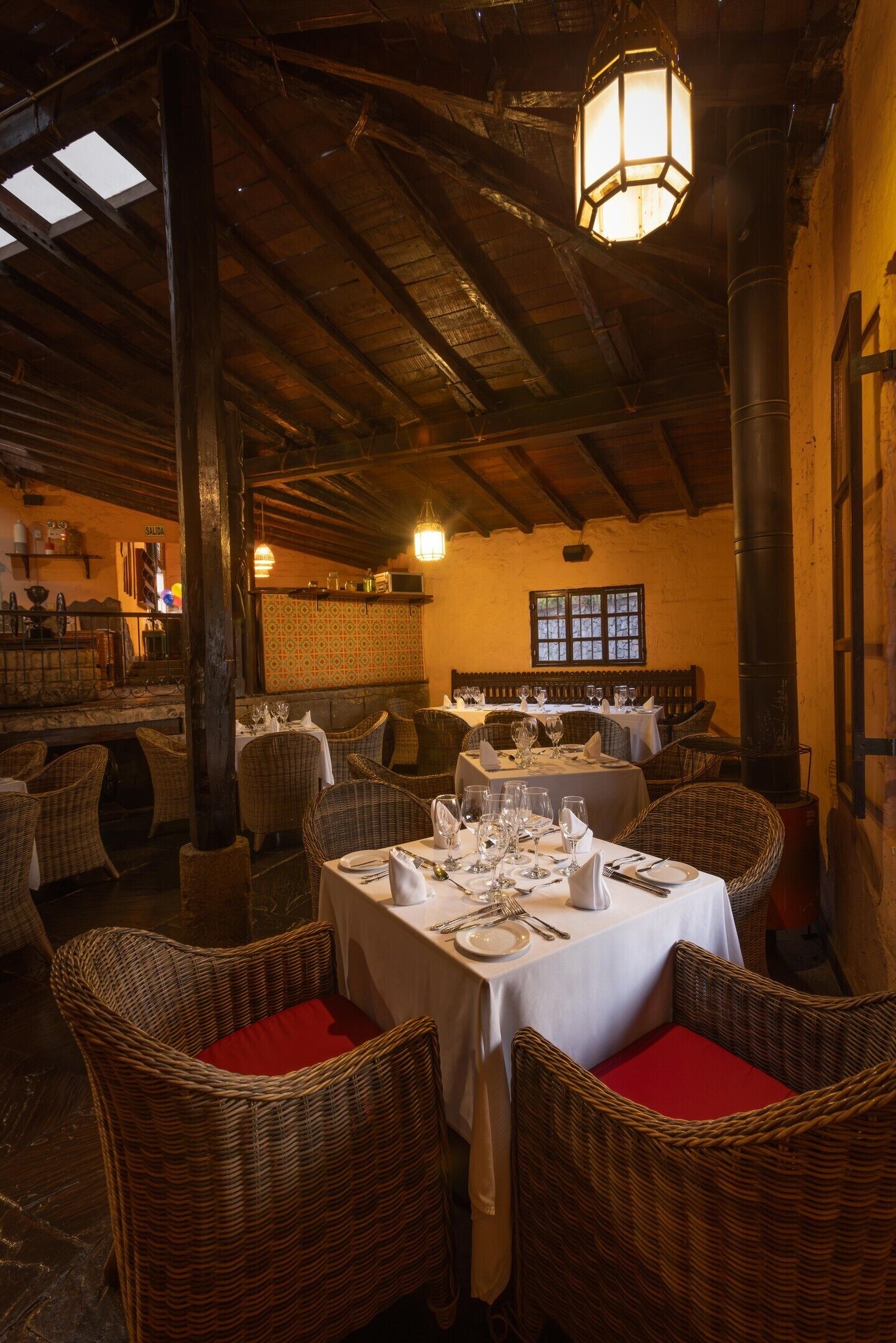 Interior de restaurante con techos altos de madera, mobiliario de mimbre y mesas dispuestas para comer.