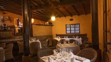 Een restaurantinterieur met hoge houten plafonds, rieten meubels en gedekte tafels.