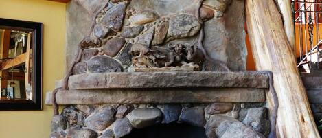 A stone fireplace with antlers, a mirror, and a patterned pillow.