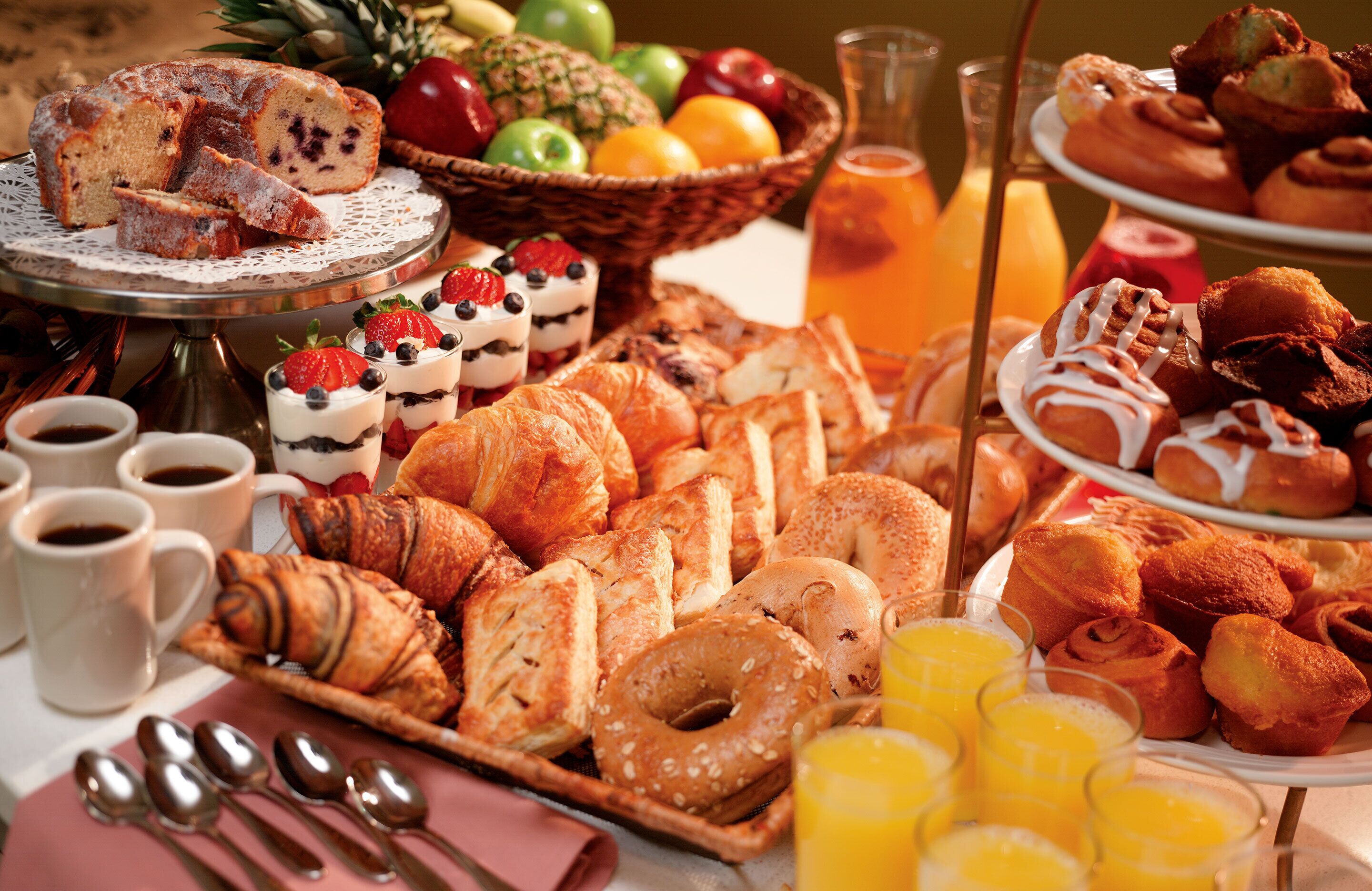 A breakfast buffet with pastries, fruits, and beverages.