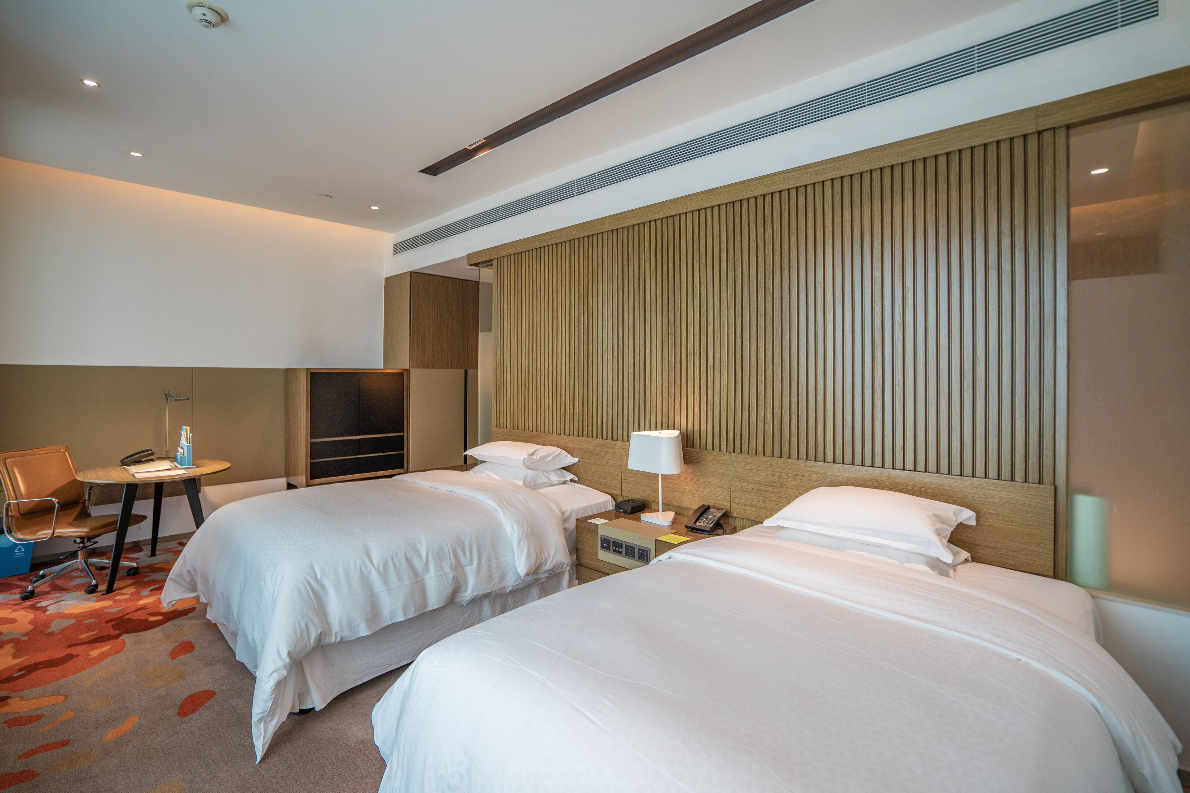 Een hotelkamer met twee bedden, een bureau, een stoel, een lamp en een telefoon.